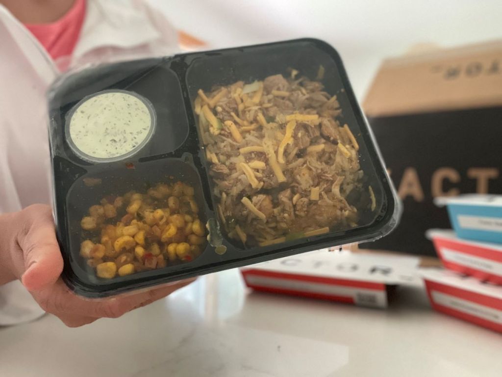 Hand holding a Factor Meal package with noodles, corn, and a dressing in it