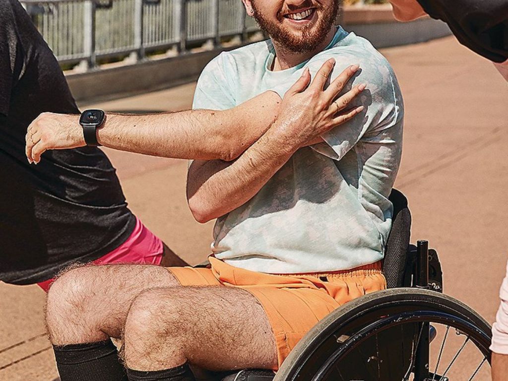 man in wheelchair wearing fitbit watch stretching his arms