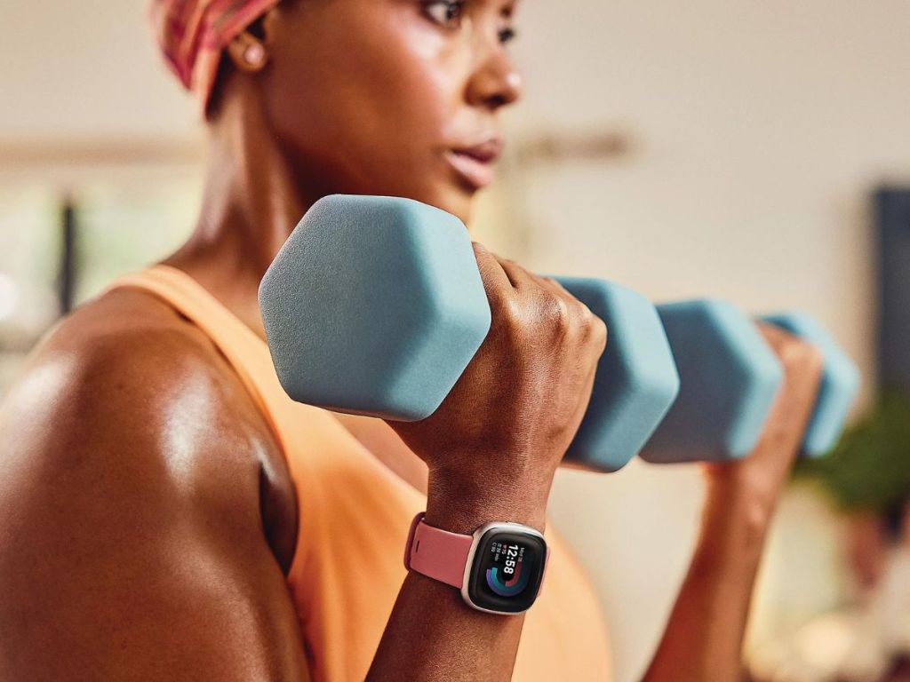 woman wearing pink Fitbit watch lifting green weights in gym