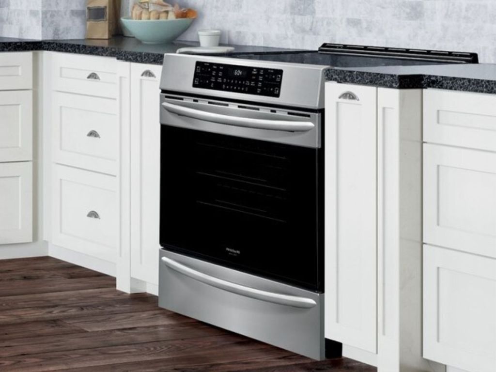Silver and black oven next to white cupboards