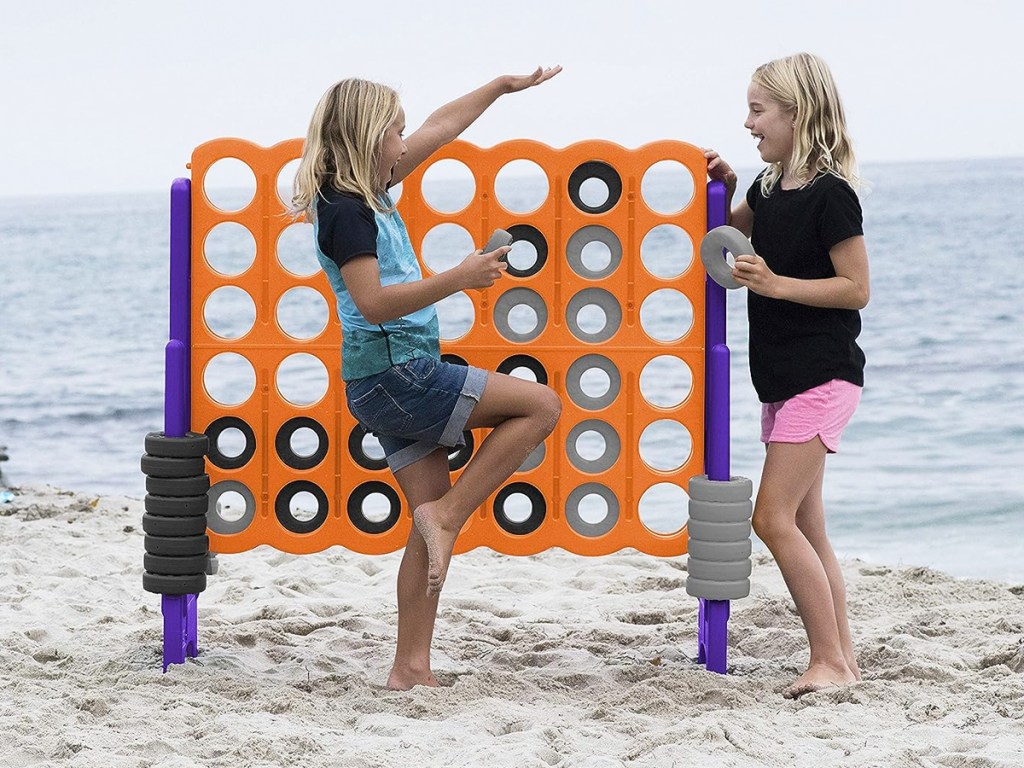 two girls at the beach playing with a giant 4-In-A-Row Game