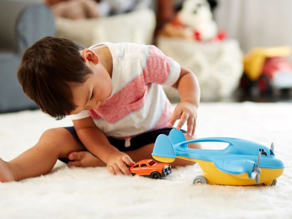 Child playing with a plastic cargo plane and car while sitting on a white carpeted floor