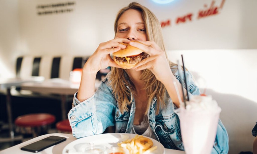 Woman eating a hamburger that she got for cheap from one of the Groupon restaurants