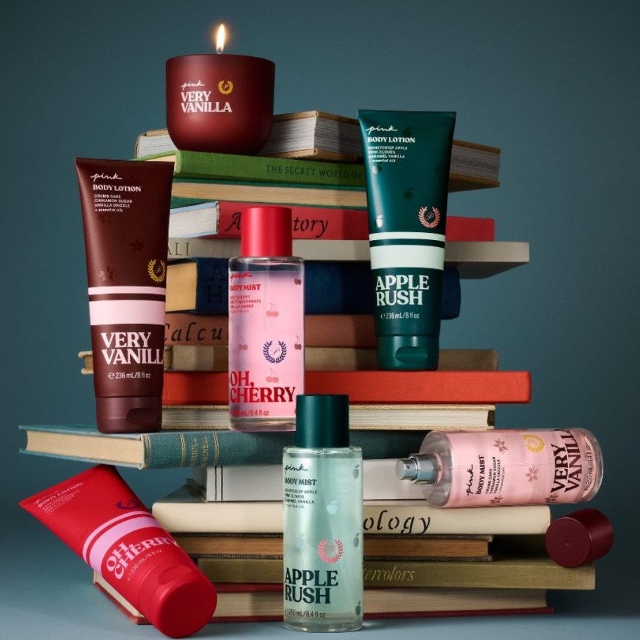 victoria's secret pink beauty items, lotion, scrubs, body mists, candles on a stack of books with a green background