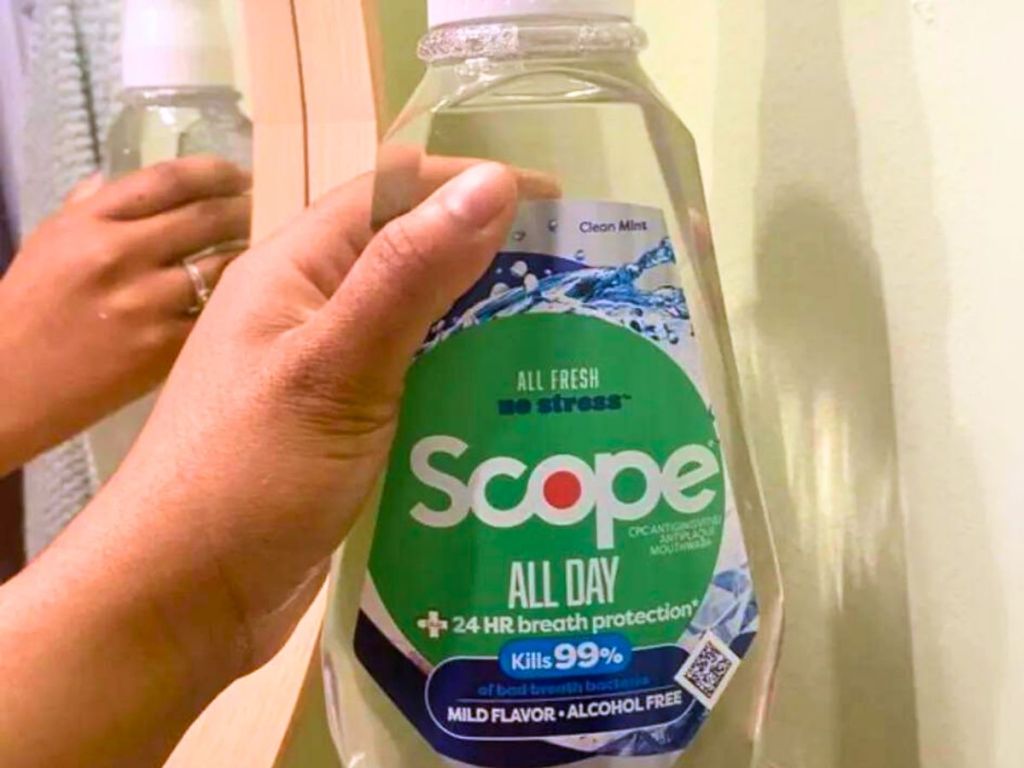 hand holding large bottle of Scope mouthwash in front of mirror 