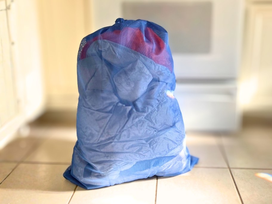 a large blue mesh laundry bag filled with clothing in a kitchen
