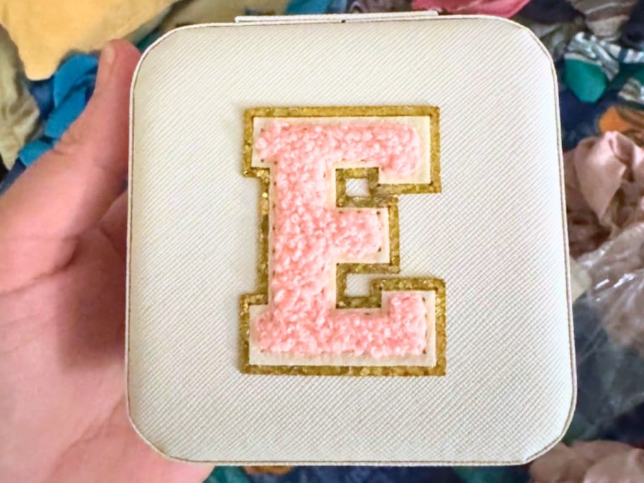 hand holding a white jewelry travel case with a pink block letter "E" on it.