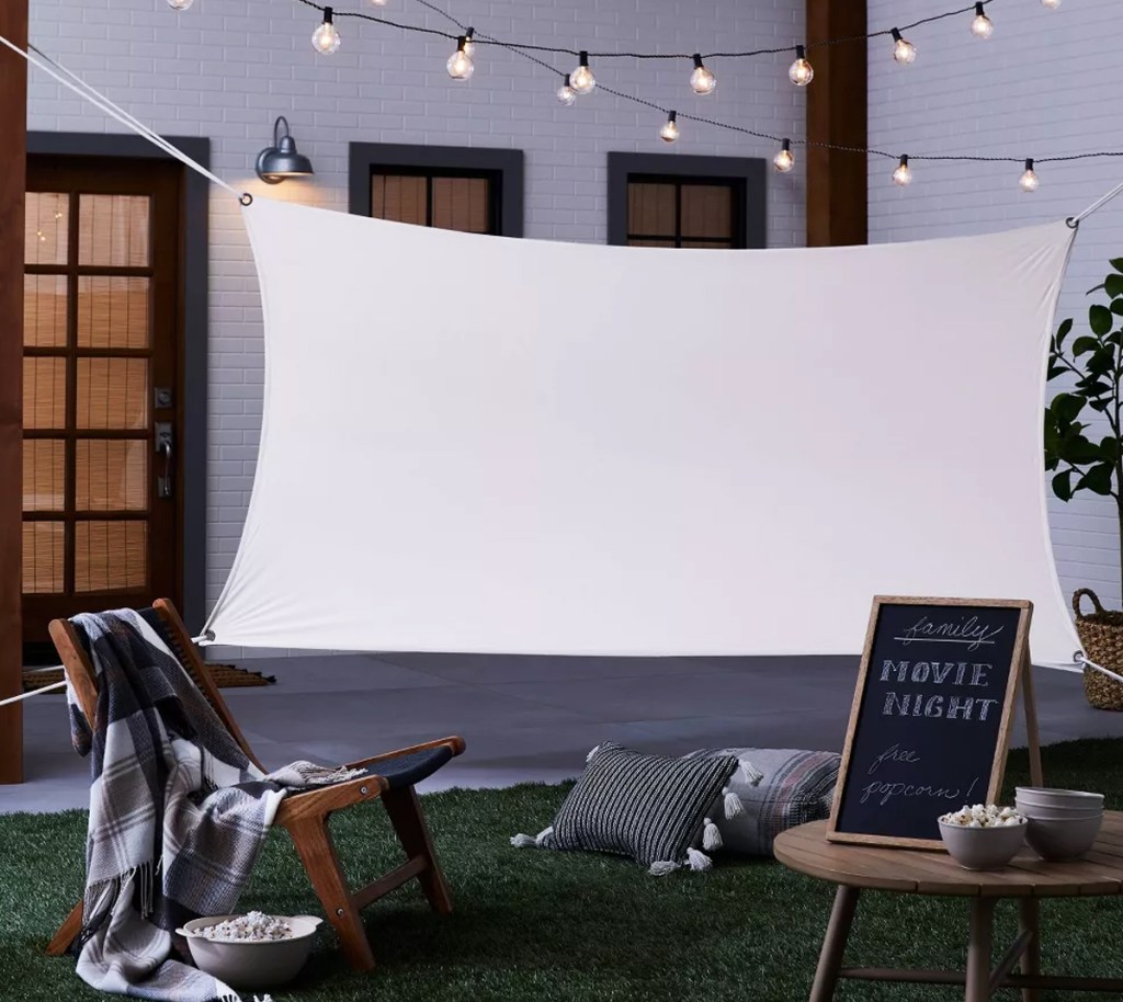 white movie screen hung in backyard with lights above it