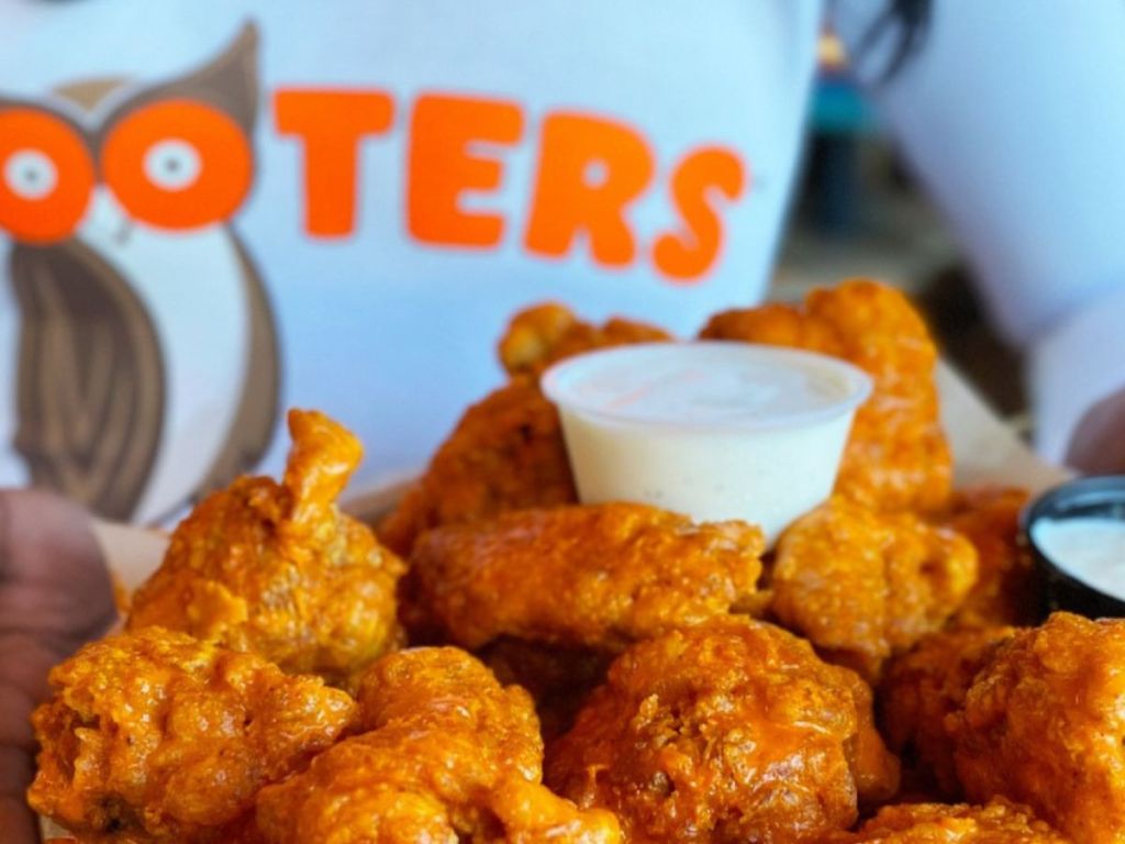pile of Hooter chicken wings with the company logo on a shirt in the background