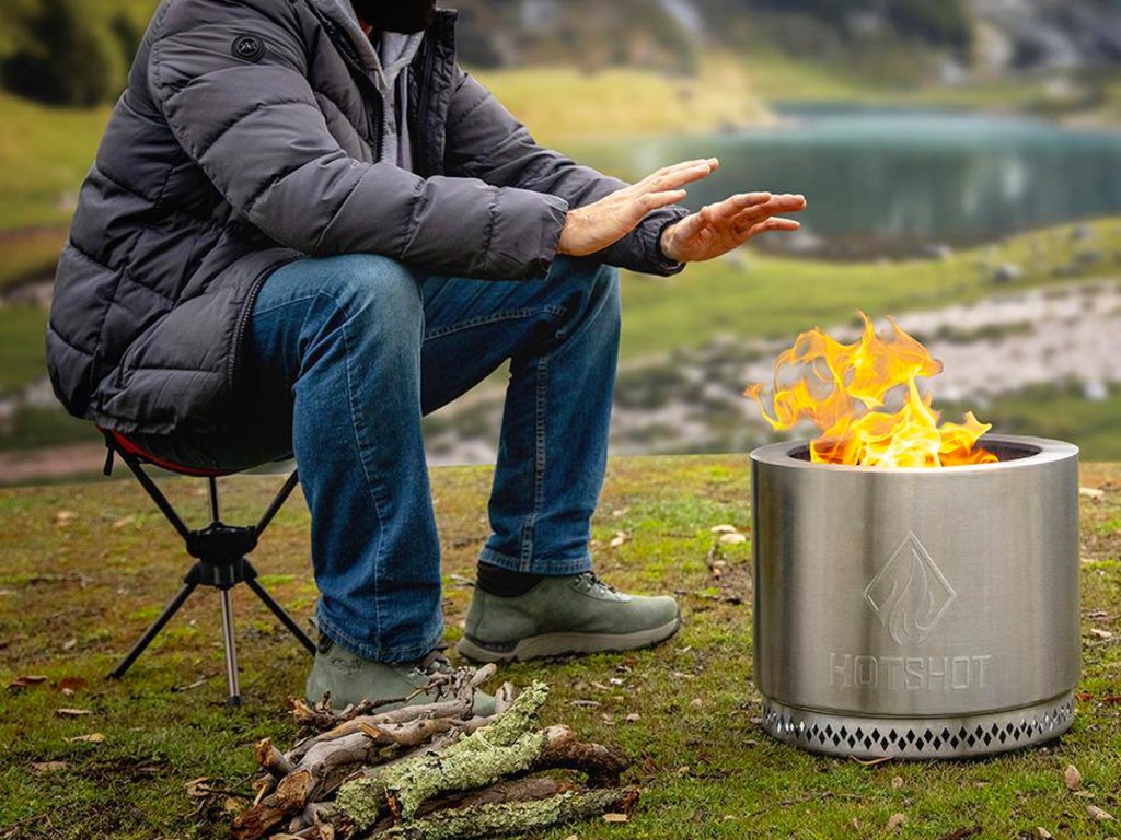 person sitting in camping chair warming hands over portable fire pit