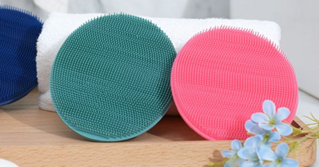 teal and pink scrubber brushes resting on towel on wood table