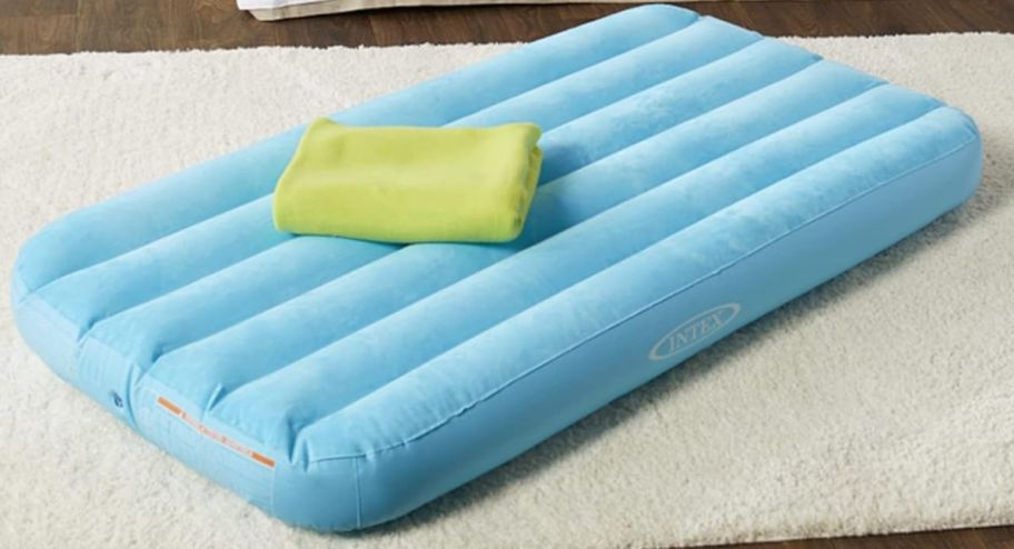 blue air mattress with a blanket on the floor on top of a rug