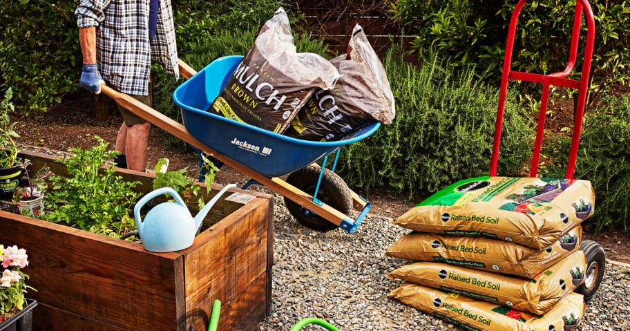 man carrying bags of mulch in wheelbarrow near stack of bags of mircale-gro garden soil