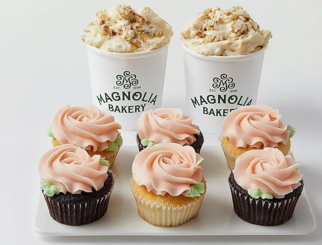 Six cupcakes with frosting on a plate and two containers of pudding behind them