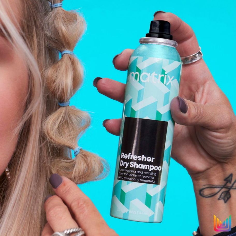 a hairstylist holding a can of matrix refresher dry shampoo and spraying it on a womans hair 