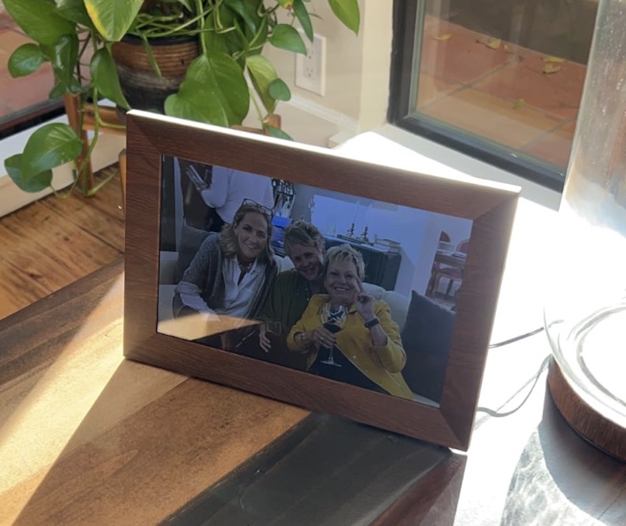 digital picture frame with brown wood frame sitting on desk next to pothos plant