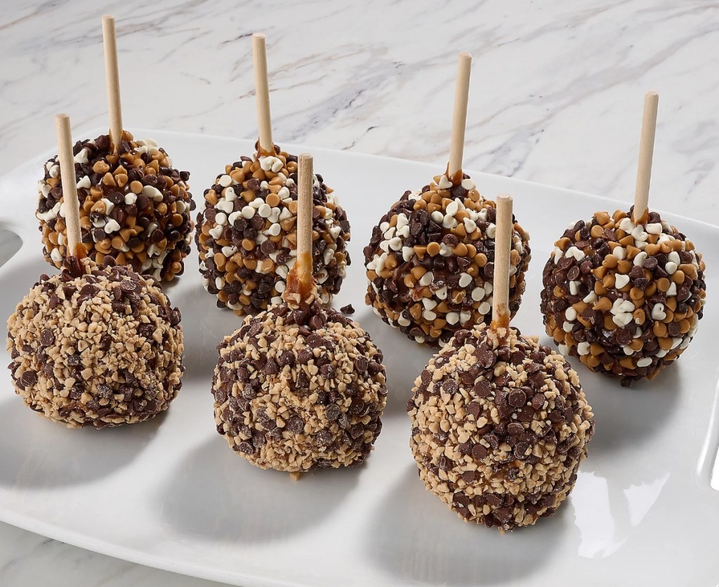 Seven caramel apples with chocolate chips on them sitting on a tray