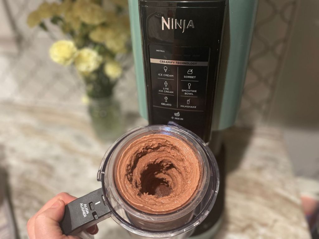 Ninja Creami with Protein Ice Cream in a pint held up in front of the machine