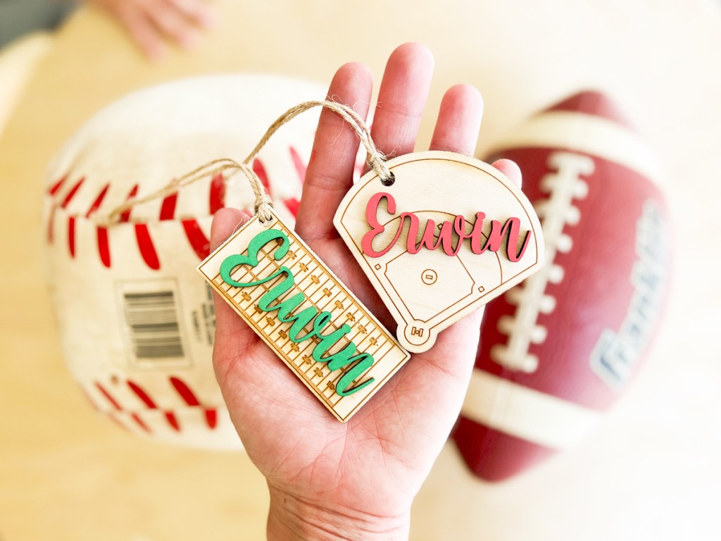 hand holding two personalized wood tags with baseball and football in background
