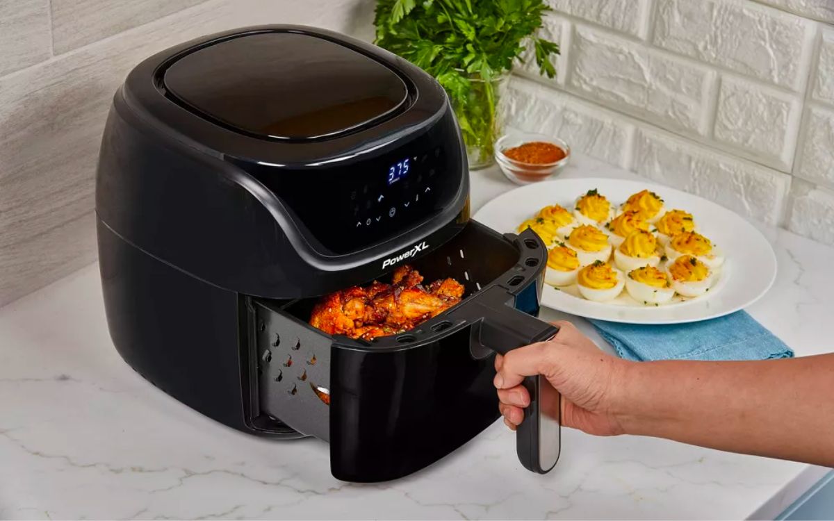 a persons hand pulling out the basket of a PowerXL Vortex Pro Air Fryer 4qt - Black with cooked food in it
