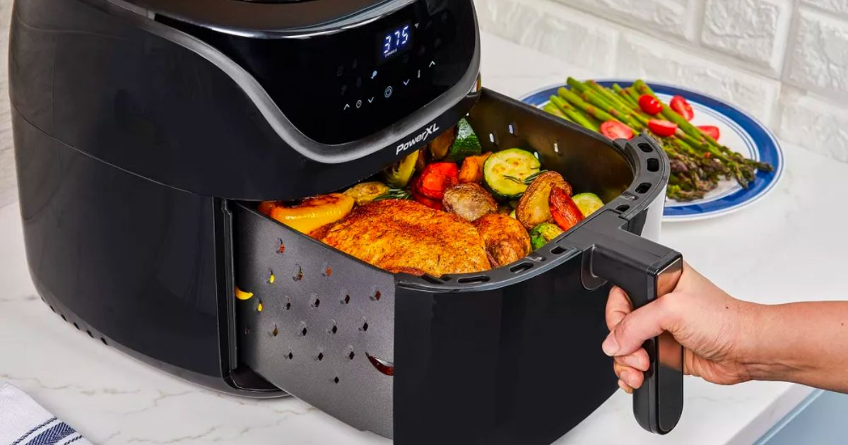 a persons hand pulling out the basket of a PowerXL Vortex Pro Air Fryer 8qt - Black with cooked food in it