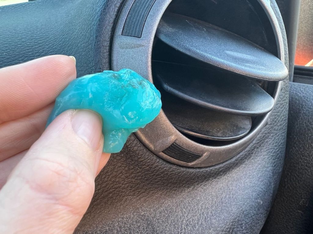 person holding a piece of blue cleaning gel next to car vent