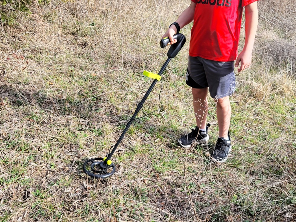 boy using a metal detector in grass