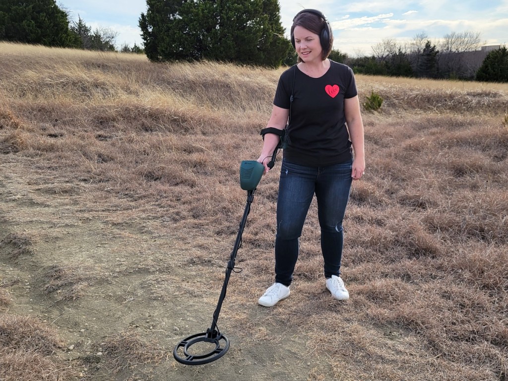 Frau benutzt einen schwarzen und grünen Metalldetektor im Feld
