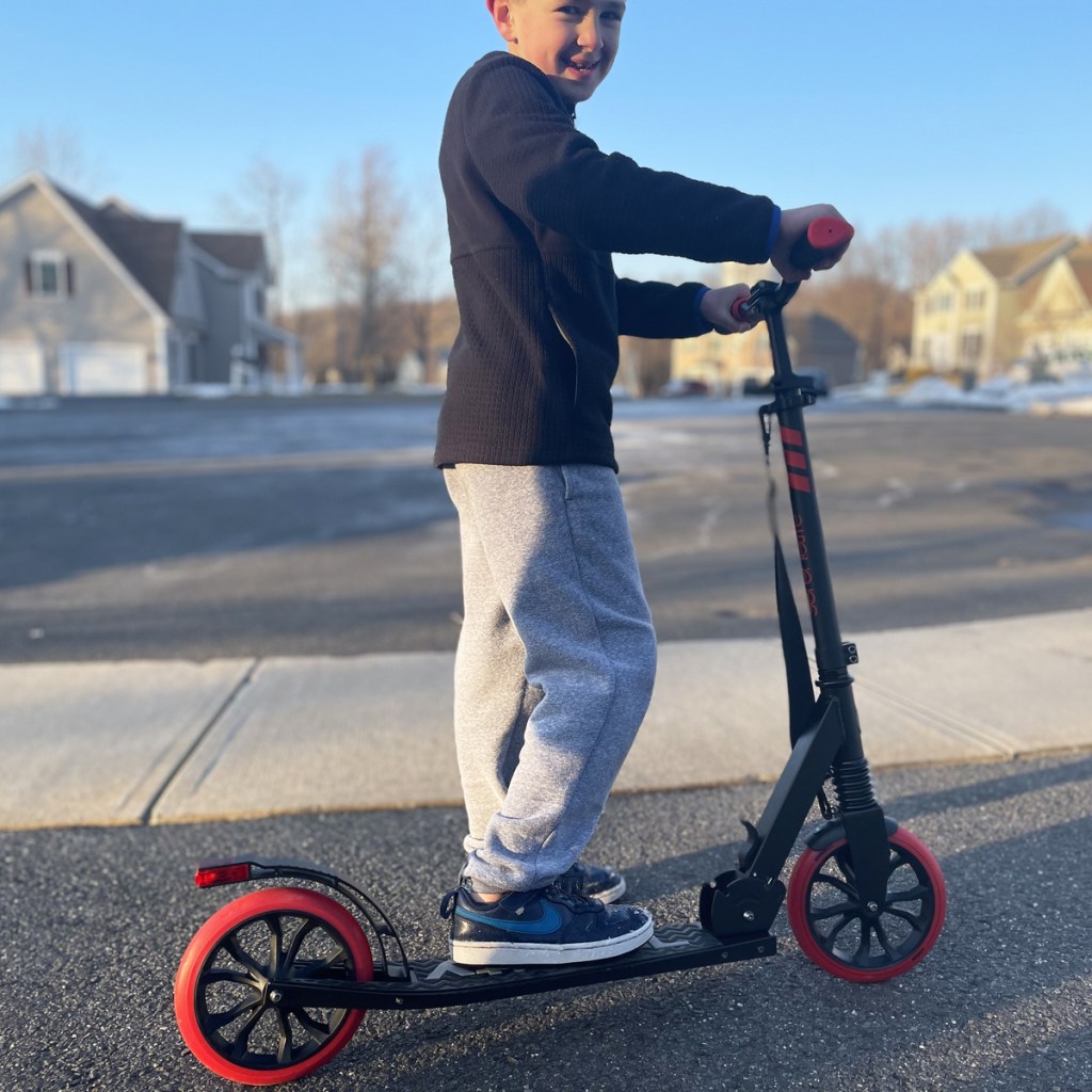 boy standing on a black and red scooter