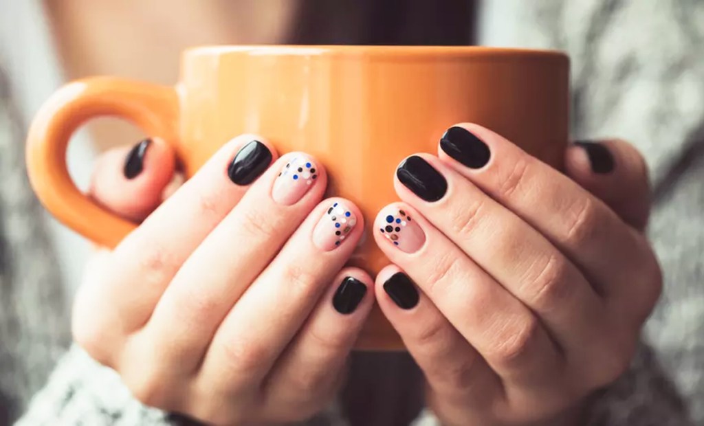 woman with black manicure holding coffee cup