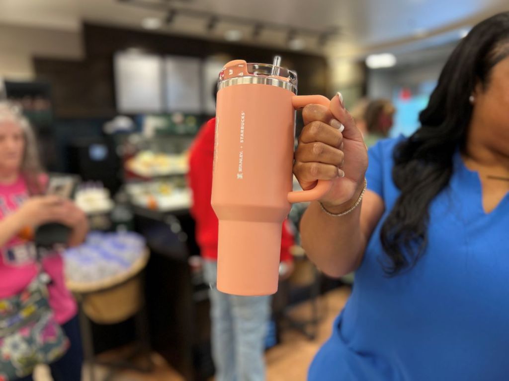 Woman holding a peach colored Stanley tumbler at Starbucks
