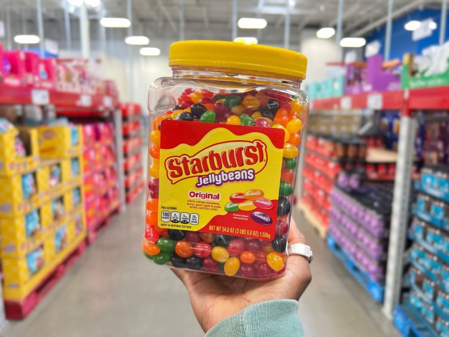 A hand holding a large jar ofStarburst Jellybeans