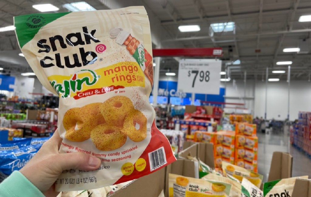 Woman holding up a bag of Snak Club Tajin Mango Rings in front of Sam's Club signage