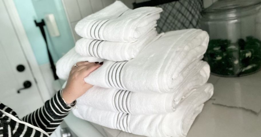 hand pulling white plush towel off stack of bath towels in bathroom