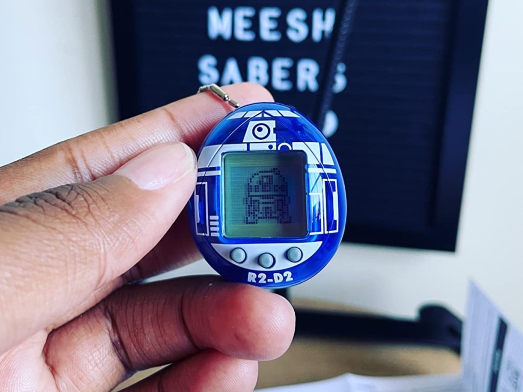 a mans hand holding a r2 d2 tamagotchi