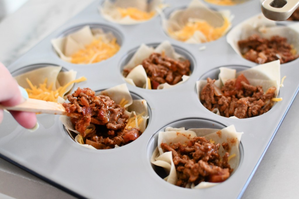 adding taco meat mixture to taco cups