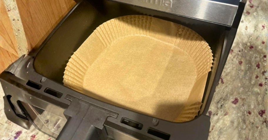an air fryer with the basket out showing a paper liner in it