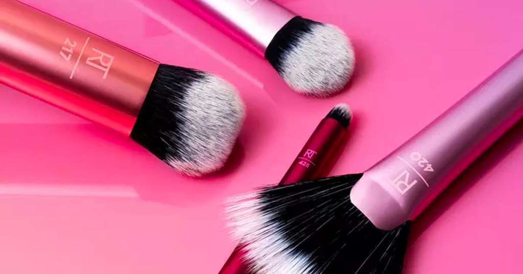4 makeup brushes laying on pink background