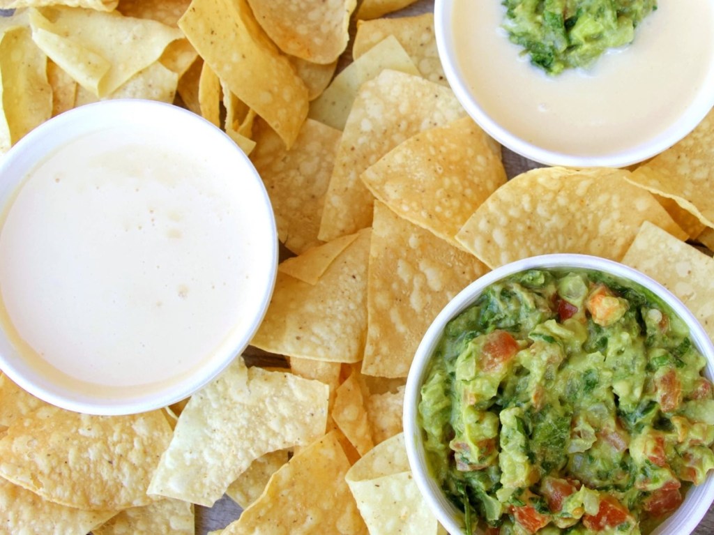 cups of queso and guacamole on pile of tortilla chips