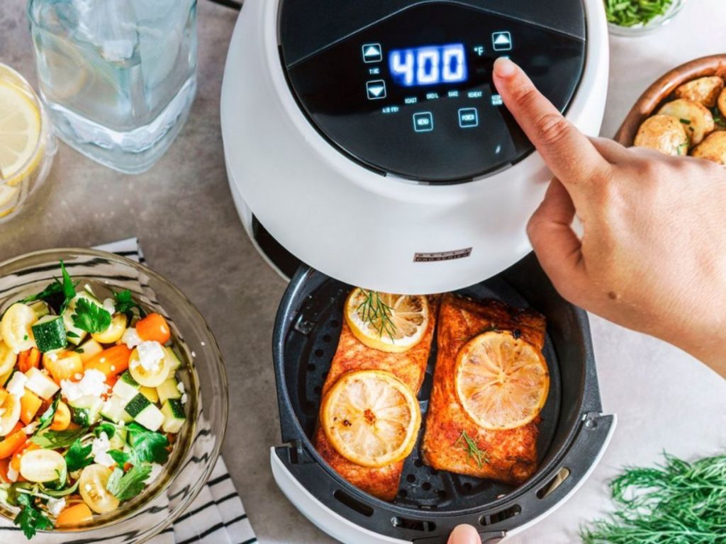 person using digital screen on white Bella air fryer containing fish with lemon