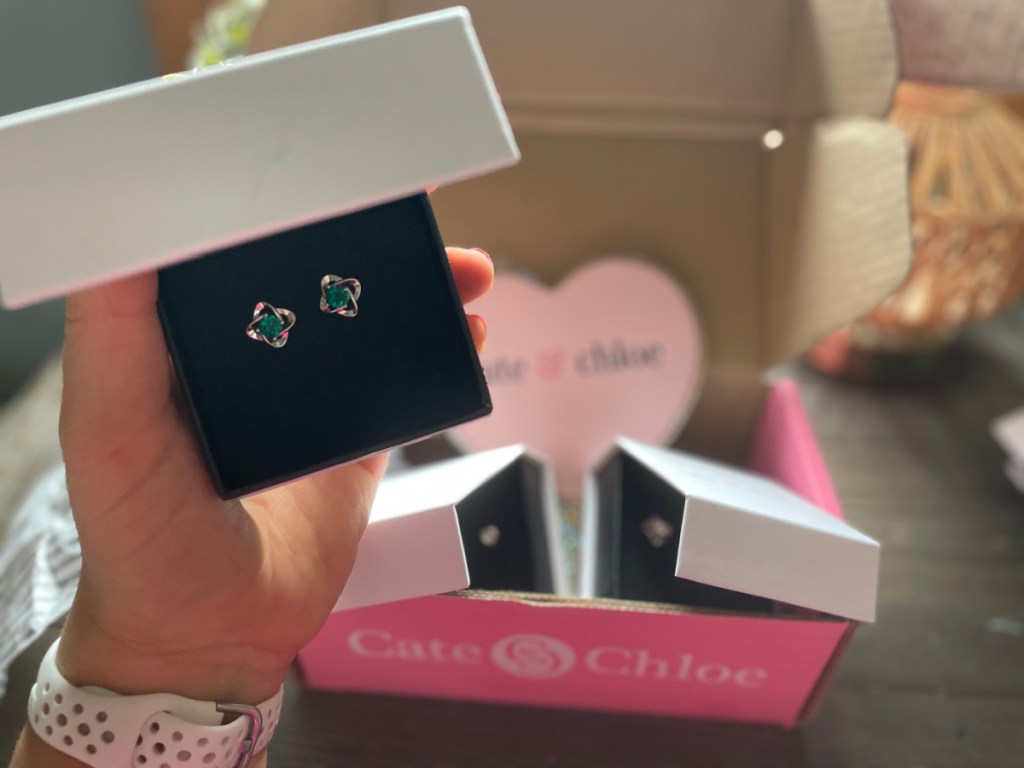 hand holding earrings in front of jewelry subscription box