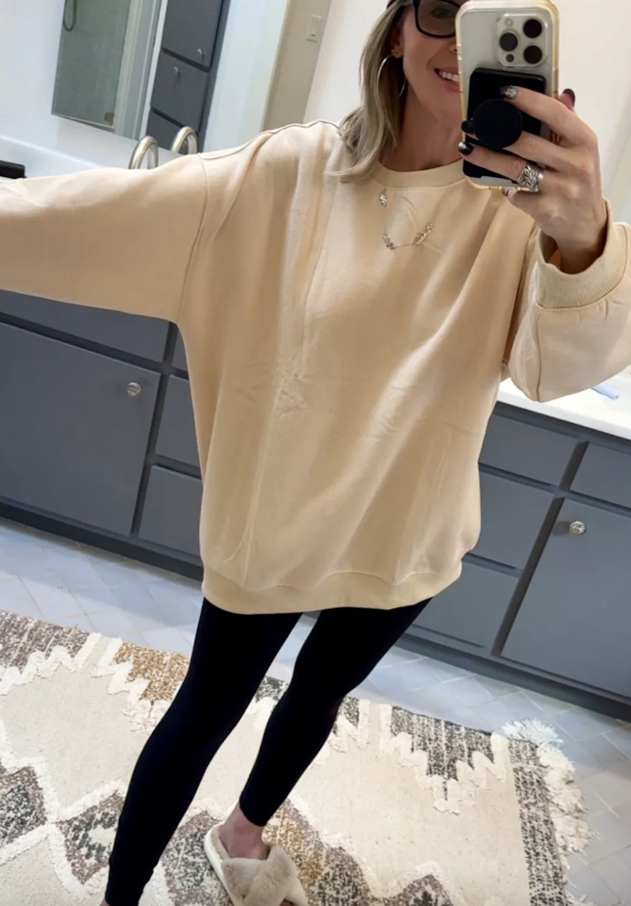 woman taking mirror selfie in oversized sweatshirt and black leggings with fuzzy slippers