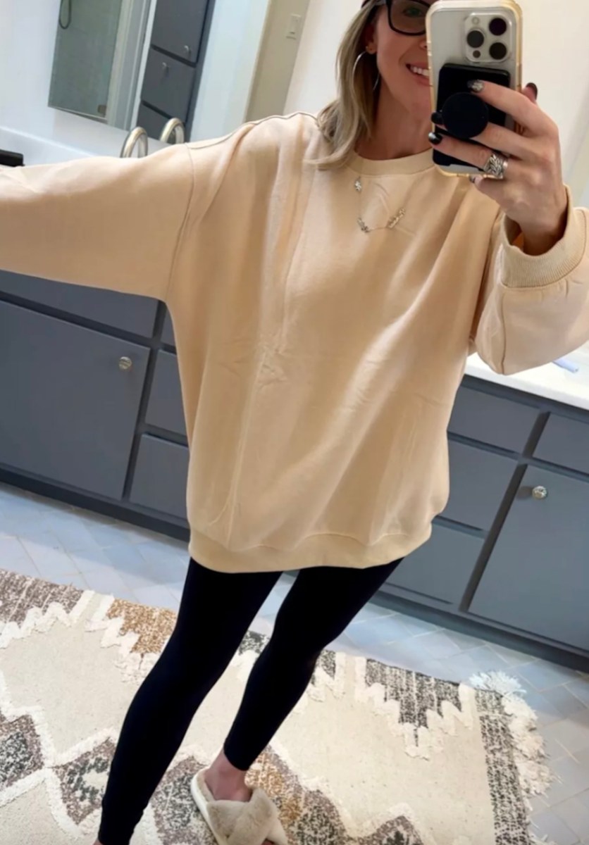 woman taking mirror selfie in oversized sweatshirt and black leggings with fuzzy slippers