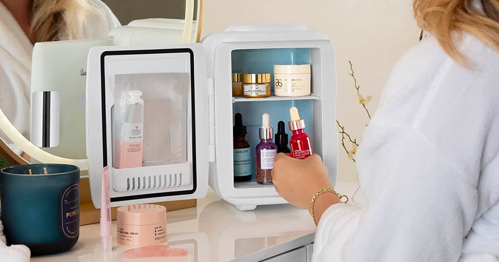 woman opening white skincare beauty fridge on table