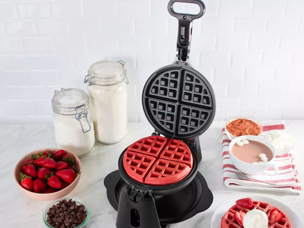 red velvet waffle in waffle maker with strawberries and toppings on side