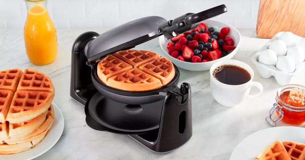 dash waffle maker with waffle inside and bowl of fruit