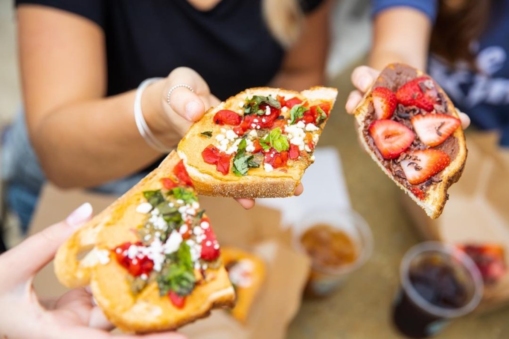 hands holding toast with various toppings