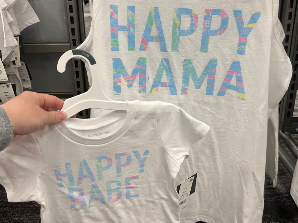 hand holding happy baby shirt in front of happy mama shirt