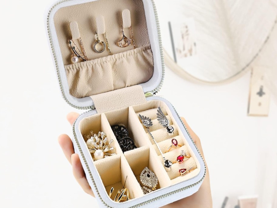 hand holding a white velvet jewelry travel case open showing jewelry inside