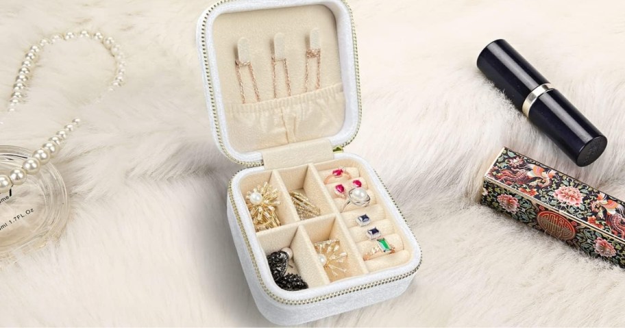 white velvet jewelry travel case open showing jewelry inside, lipstick next to it